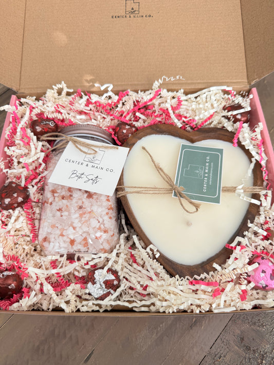 Close up Top view of open Valentine's Gift box featuring Wooden Heart Bowl luxury candle with epsom bath salts and dove chocolates. 