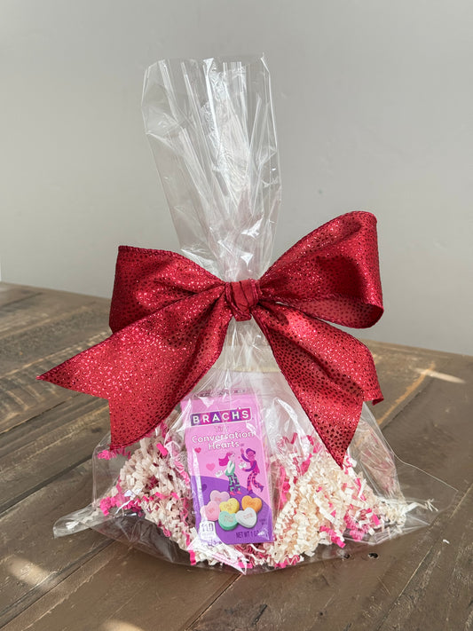 Secret message candle and package of conversation hearts wrapped in a gift bag.  Front View